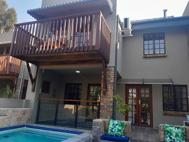 Rear exterior view featuring a swimming pool, a covered patio area, and an upper-level balcony with timber railings.