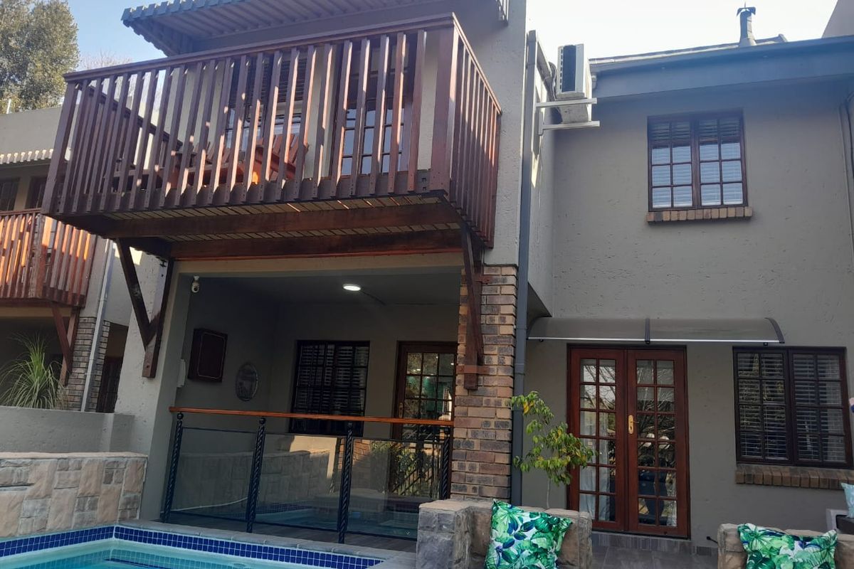 Rear exterior view featuring a swimming pool, a covered patio area, and an upper-level balcony with timber railings.