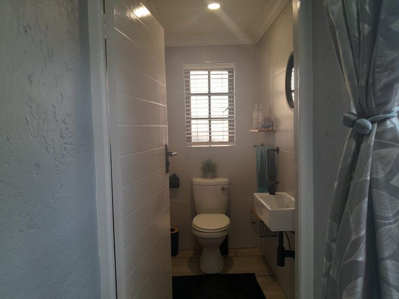 A compact, modern bathroom featuring a wall-mounted basin, toilet, and neutral tiled finishes, presented in a clean and functional condition.