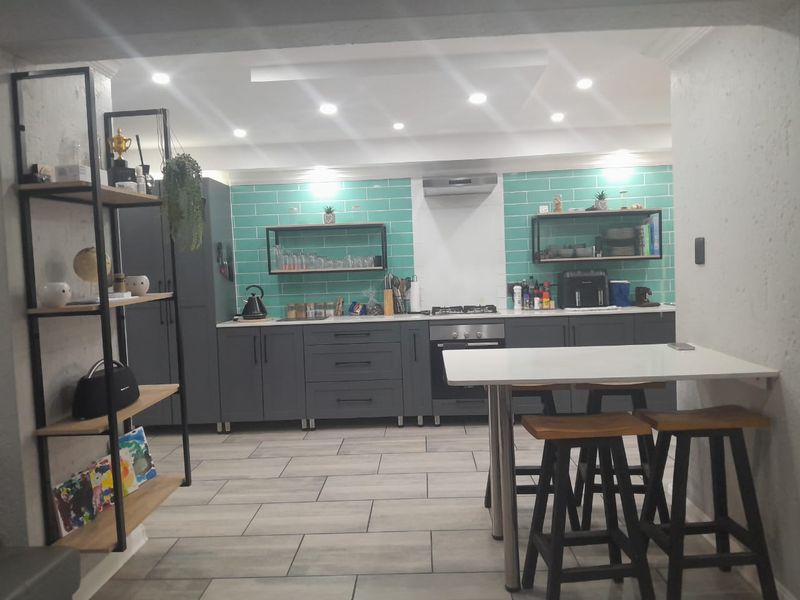 Modern kitchen featuring dark grey cabinetry, vibrant teal subway tile backsplash, gas hob, built-in oven, and integrated breakfast bar area with recessed lighting.