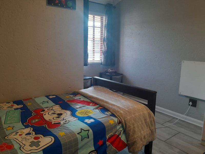A functional bedroom featuring tiled flooring and a window with venetian blinds, providing a neutral space ready for personalization.