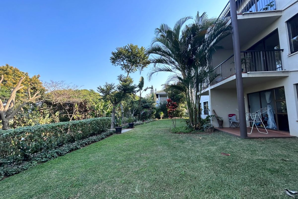 A view of the rear garden and lawn area, featuring a covered patio and upper-level balconies with metal railings.