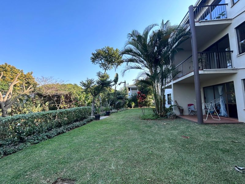 A view of the rear garden and lawn area, featuring a covered patio and upper-level balconies with metal railings.