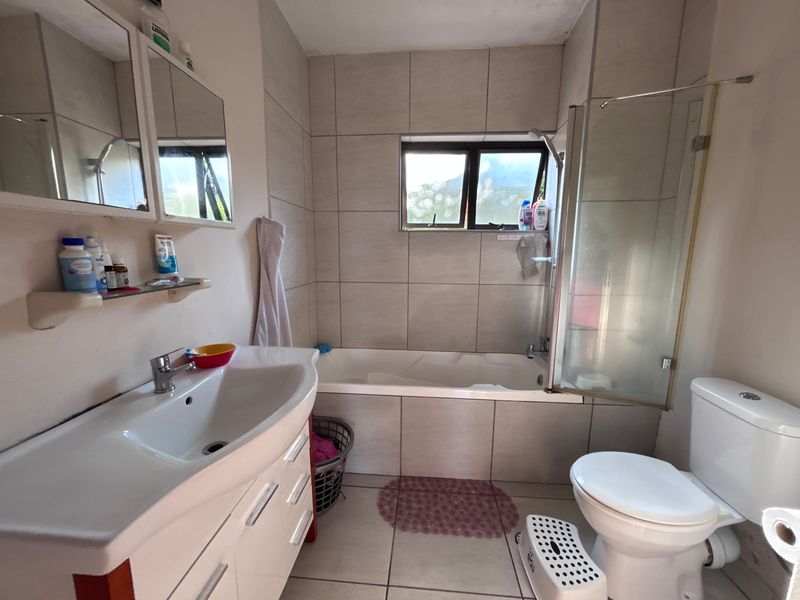 A functional bathroom featuring a vanity with basin, a bathtub with a glass shower screen, and a standard toilet with neutral wall and floor tiling.