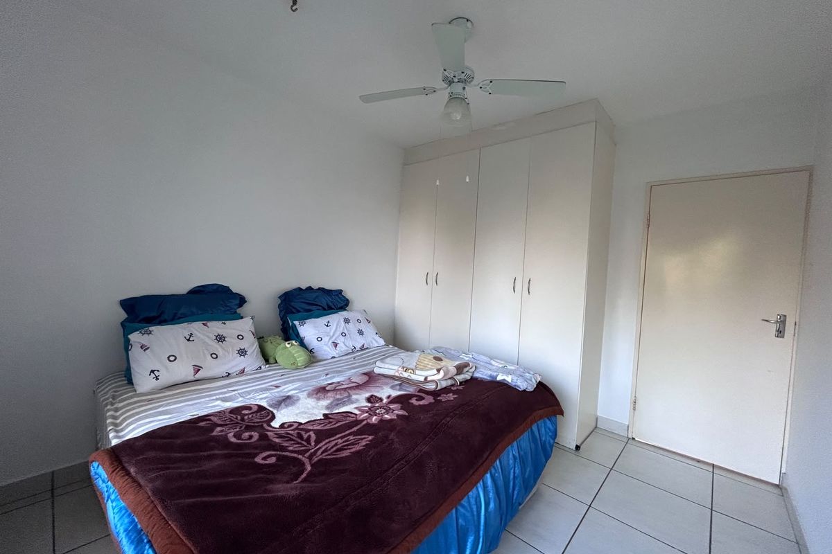 A functional bedroom featuring tiled flooring, a ceiling fan, and built-in cupboards for storage.