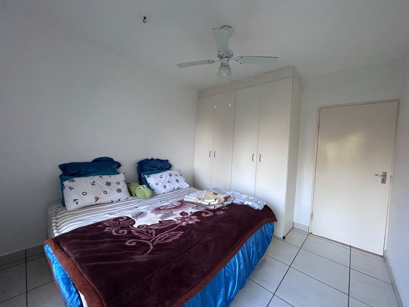 A functional bedroom featuring tiled flooring, a ceiling fan, and built-in cupboards for storage.