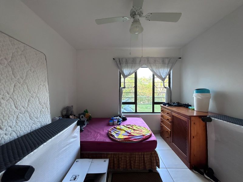 A bedroom featuring tiled flooring, a ceiling fan, and a window with security bars, offering a functional space for rest.