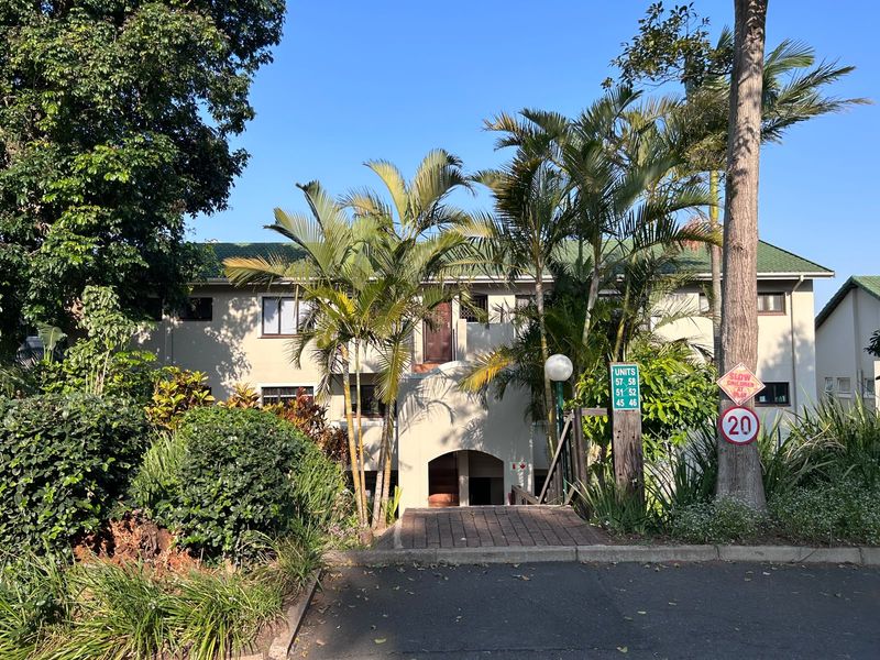 Front elevation of an apartment complex featuring a paved entrance walkway, established palm trees, and landscaped garden surroundings.