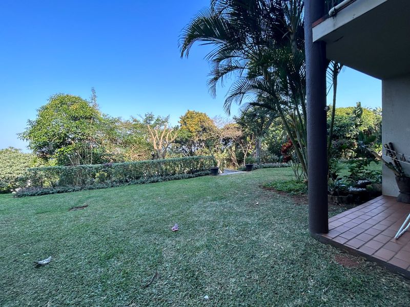 A well-maintained private garden area featuring a tiled patio space, lush lawn, and established perimeter hedging.