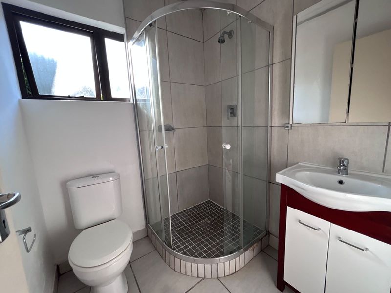 A functional bathroom featuring a corner shower enclosure, a vanity unit with a washbasin, and a standard toilet with neutral wall and floor tiling.