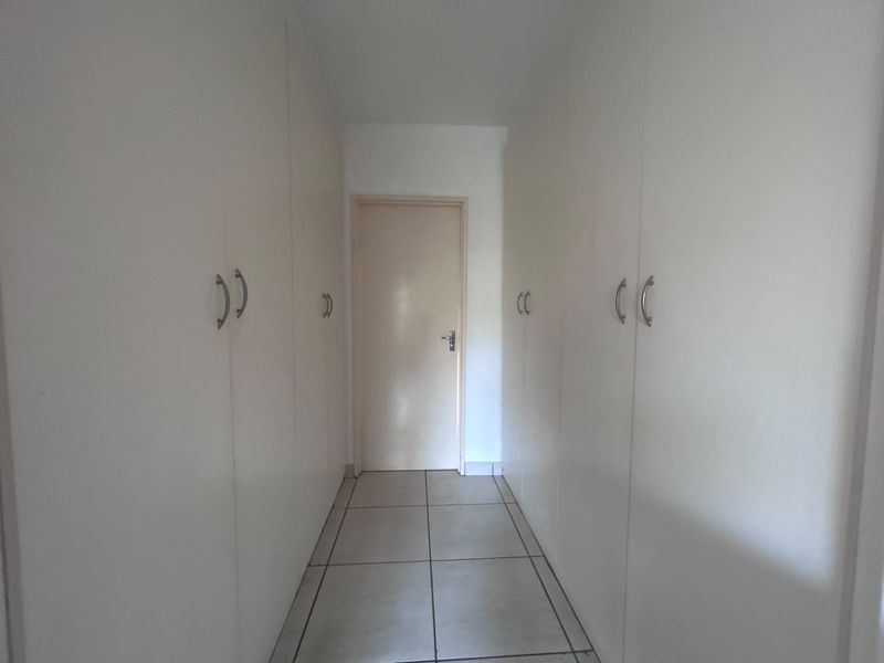 A functional hallway featuring extensive built-in storage cupboards and neutral tiled flooring, providing a clean and organized transition space.