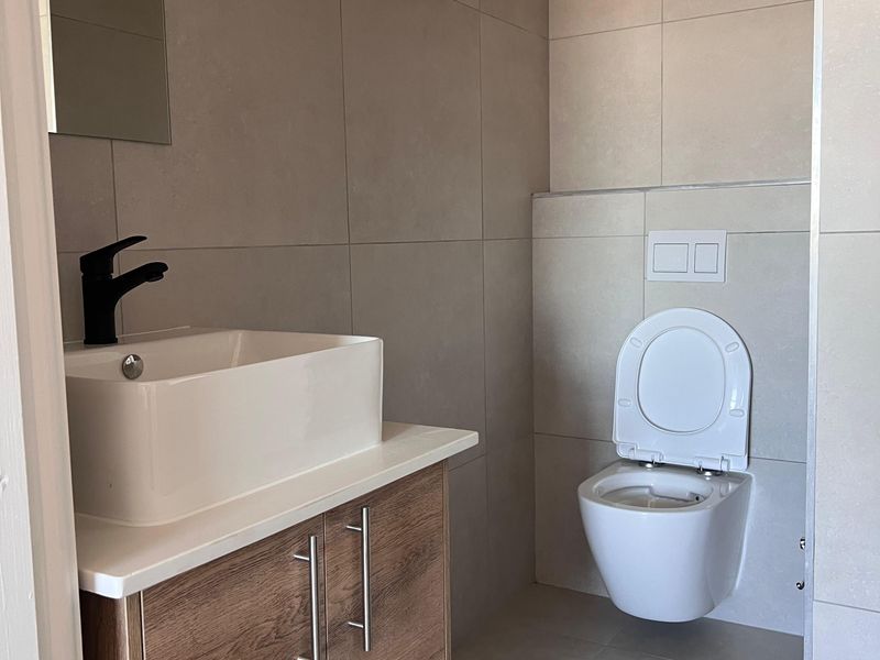 Modern bathroom featuring a wall-mounted toilet, vanity cabinet with a vessel sink, black mixer tap, and neutral floor-to-ceiling tiling.