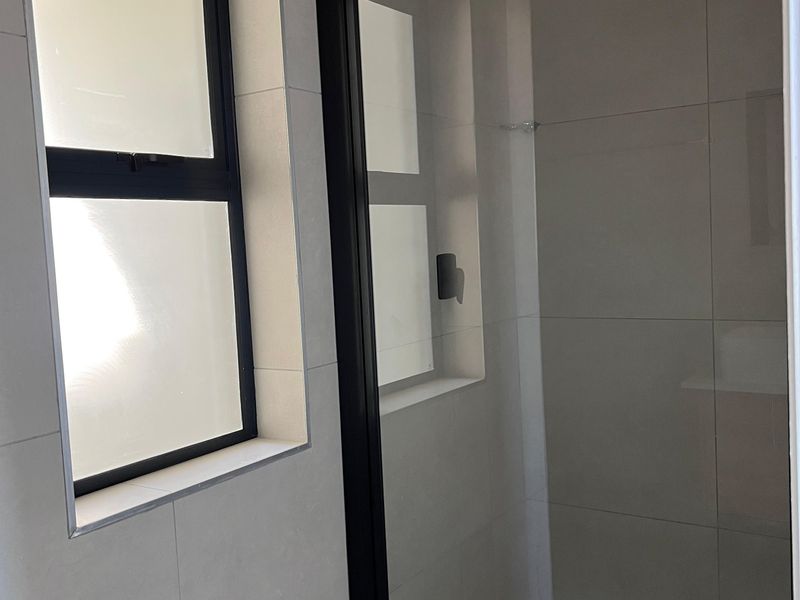 Modern bathroom featuring a walk-in shower with a sleek black-framed glass enclosure, rain shower head, and neutral wall tiling.