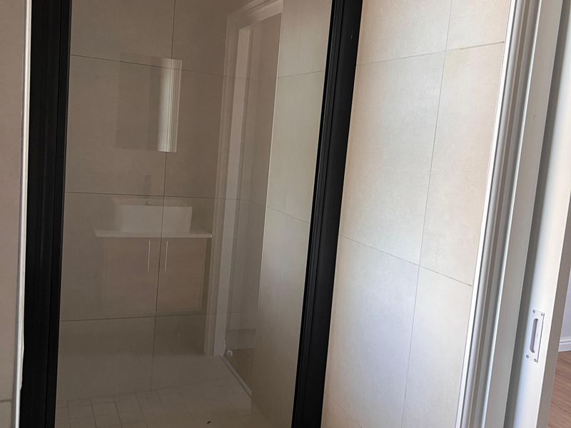 Modern bathroom featuring a walk-in shower with a sleek black-framed glass screen, rain shower head, and neutral wall and floor tiling.