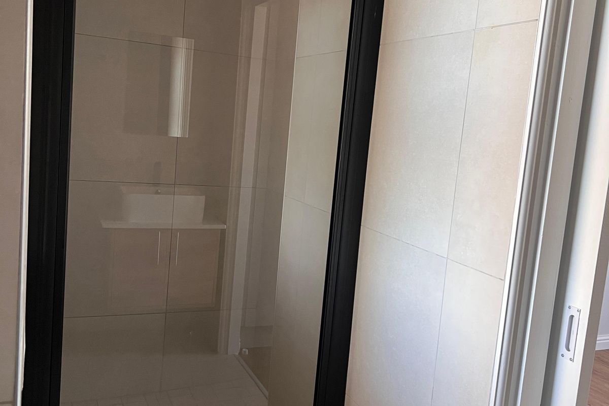 Modern bathroom featuring a walk-in shower with a sleek black-framed glass screen, rain shower head, and neutral wall and floor tiling.
