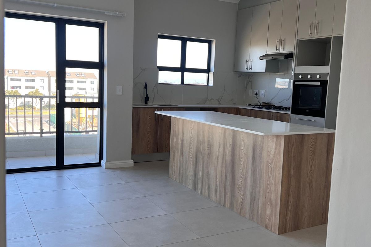 Modern open-plan kitchen featuring a central island, built-in oven, sleek cabinetry, and tiled flooring, with direct access to a private balcony.