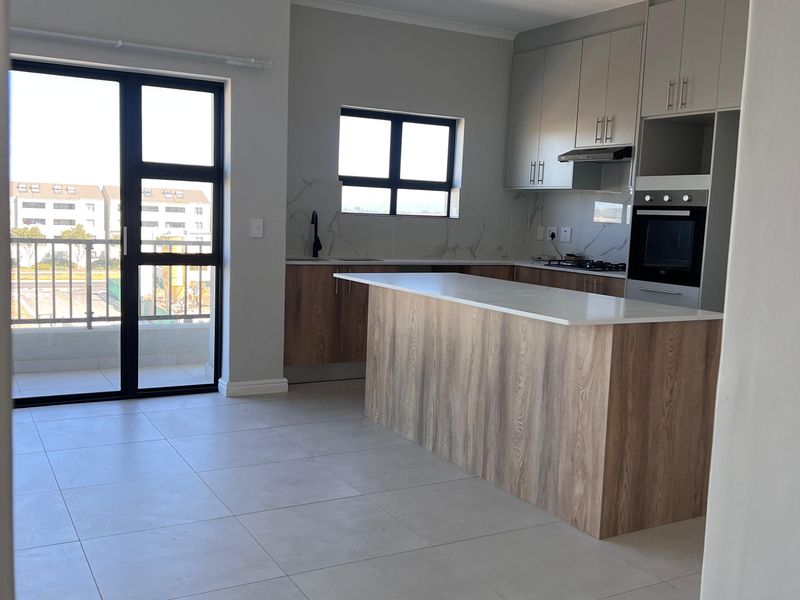 Modern open-plan kitchen featuring a central island, built-in oven, sleek cabinetry, and tiled flooring, with direct access to a private balcony.