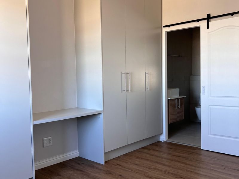 A bright, modern bedroom featuring built-in cupboards, a integrated desk, and a sliding barn door leading to an en-suite bathroom.