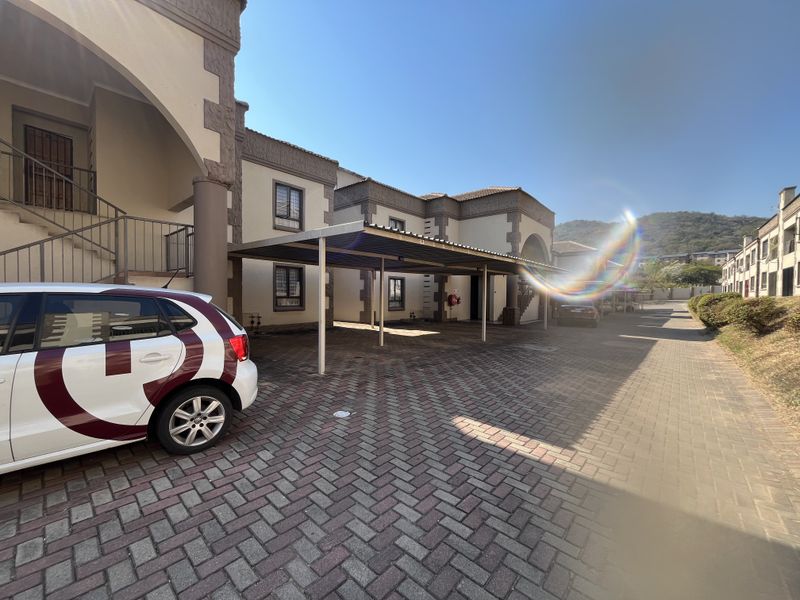 Exterior view of the apartment complex featuring a paved driveway, covered carport parking, and access staircases to upper-level units.