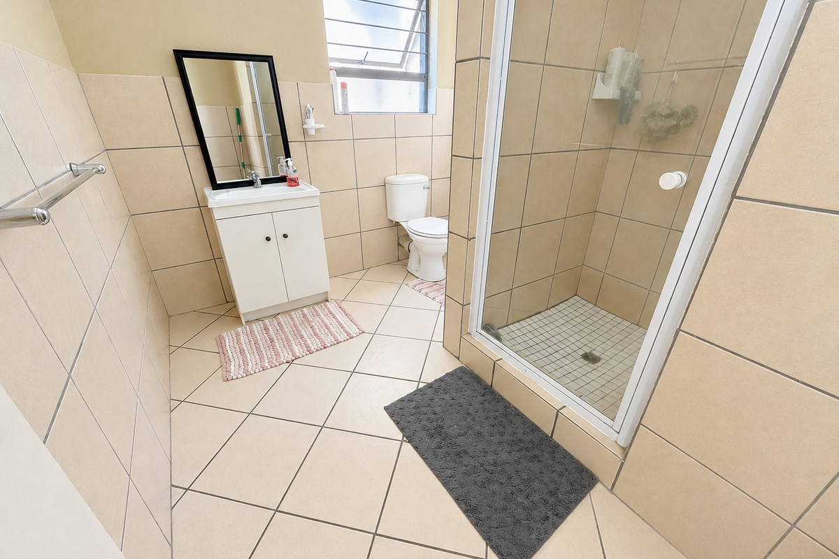 A functional bathroom featuring a vanity cabinet, toilet, and a glass-enclosed shower with neutral wall and floor tiling.