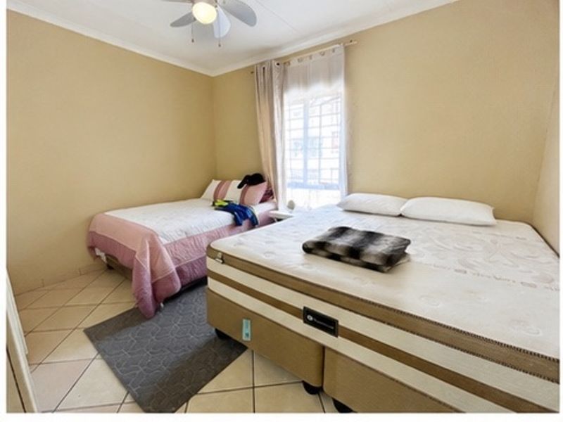 A bedroom featuring tiled flooring, a ceiling fan, and a window fitted with security bars.