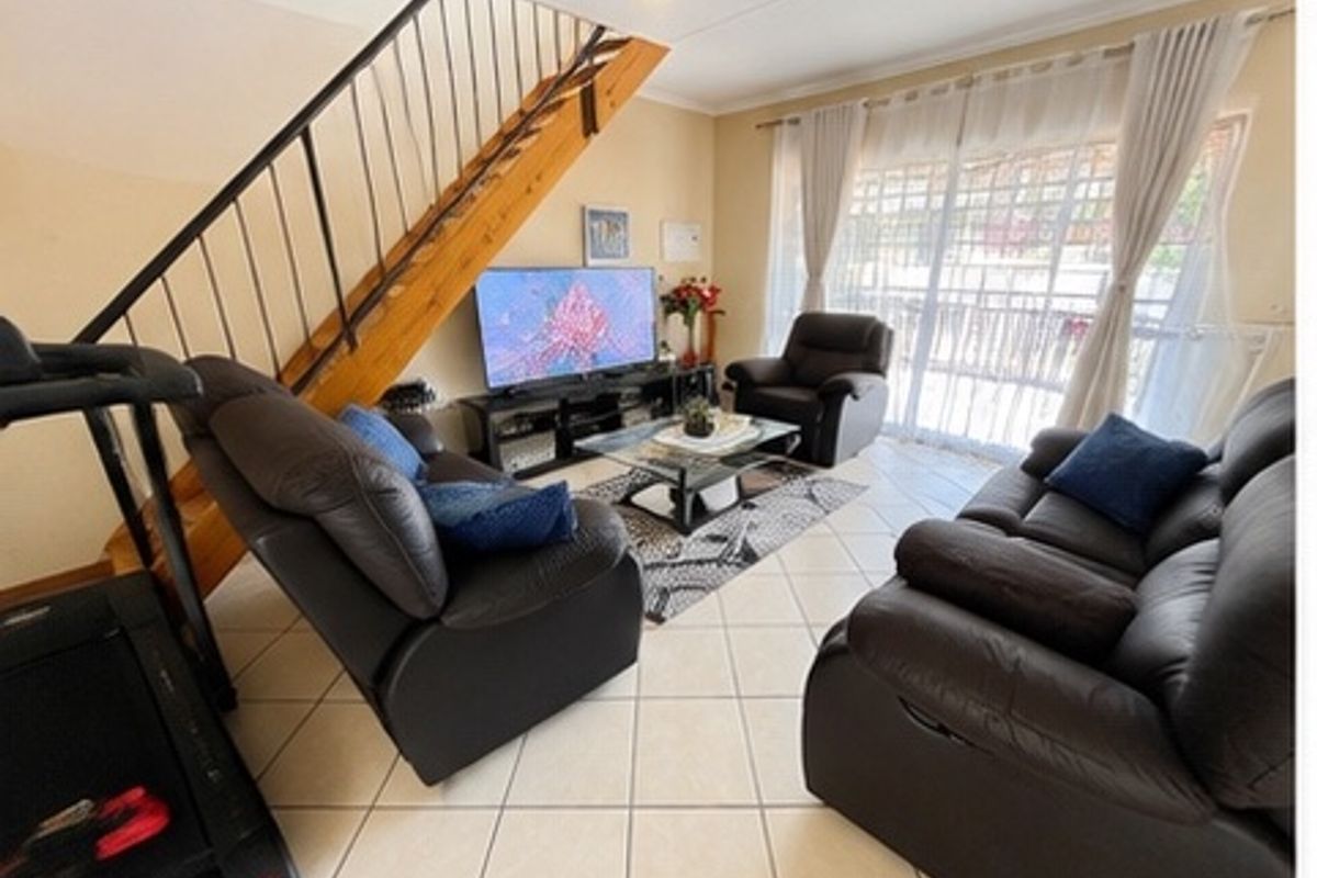 A living room featuring tiled flooring, a staircase with a metal balustrade, and a sliding glass door providing access to the exterior.