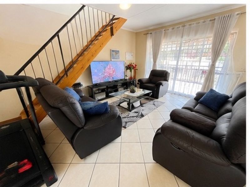A living room featuring tiled flooring, a staircase with a metal balustrade, and a sliding glass door providing access to the exterior.