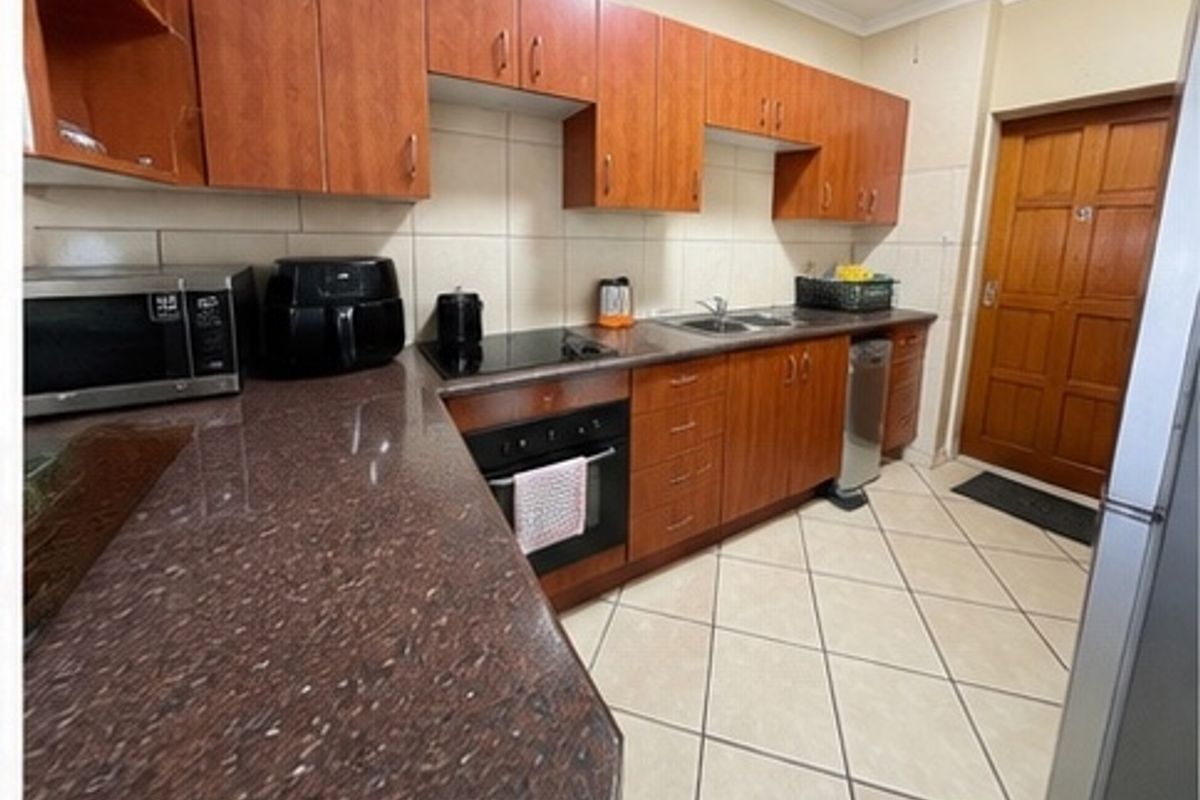 A functional kitchen featuring wooden cabinetry, granite countertops, a built-in oven, electric hob, and tiled flooring with a neutral backsplash.