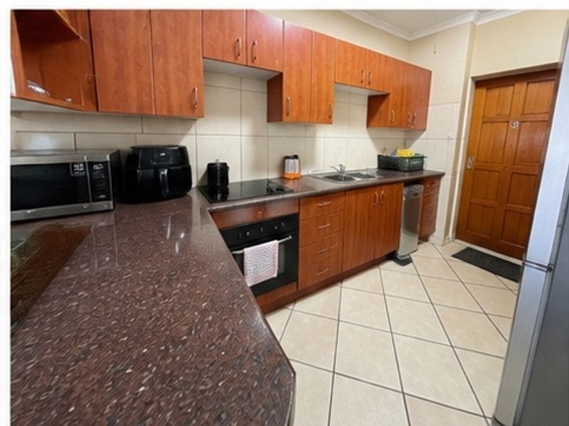 A functional kitchen featuring wooden cabinetry, granite countertops, a built-in oven, electric hob, and tiled flooring with a neutral backsplash.