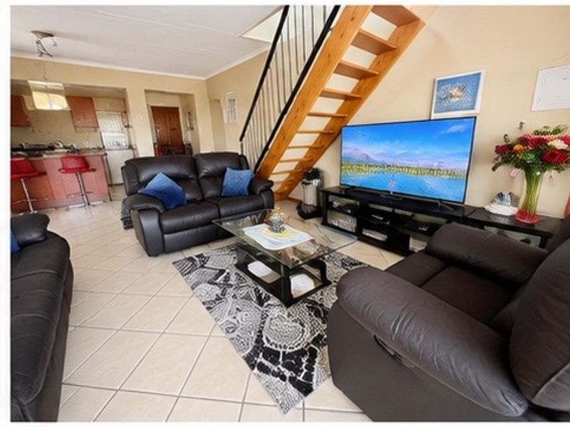 Open-plan living area featuring tiled flooring and a wooden staircase with a metal balustrade, leading to an adjacent kitchen with breakfast bar.