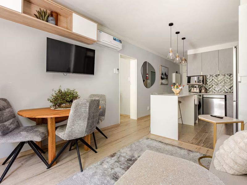 Modern open-plan living area featuring a compact kitchen with a breakfast island, herringbone backsplash, and light wood-look flooring throughout.