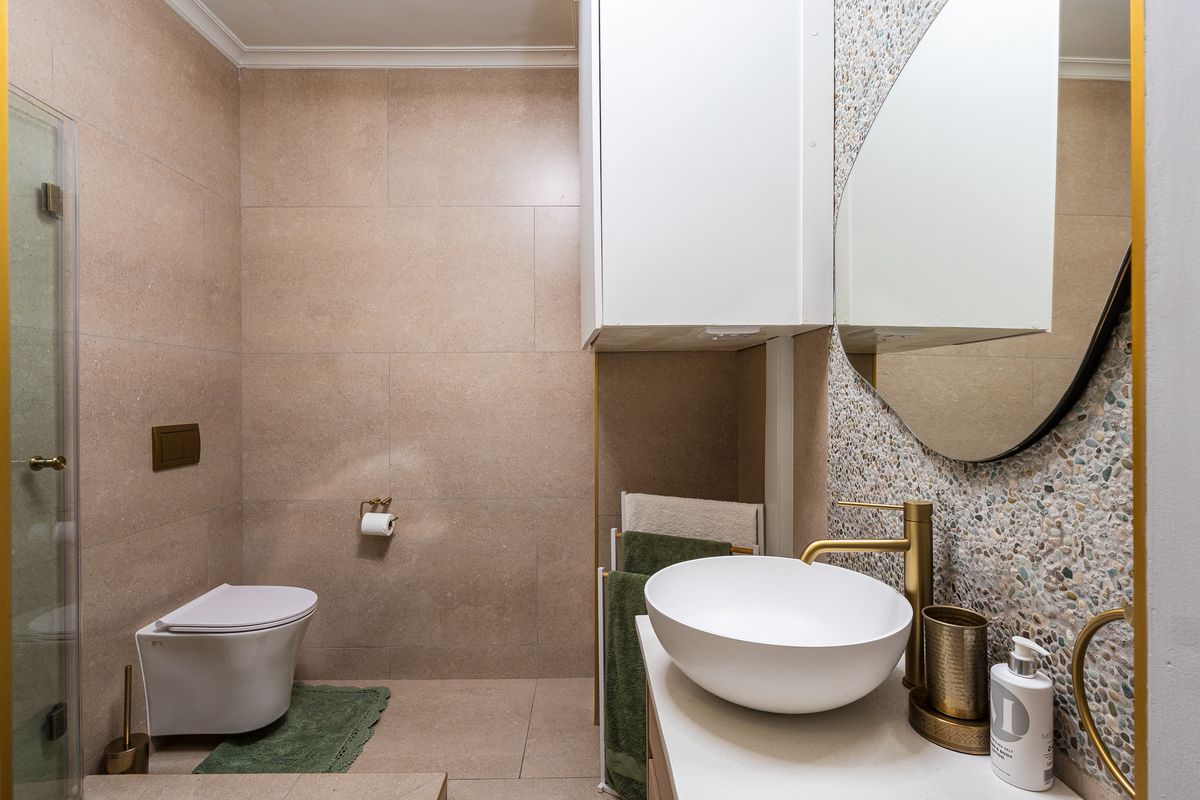 Modern bathroom featuring a wall-mounted toilet, vessel sink with brass fixtures, glass shower enclosure, and contemporary tiled finishes.
