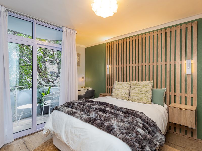 A well-appointed bedroom featuring a decorative timber slat headboard, integrated bedside tables, and direct access to a private balcony through sliding glass doors.