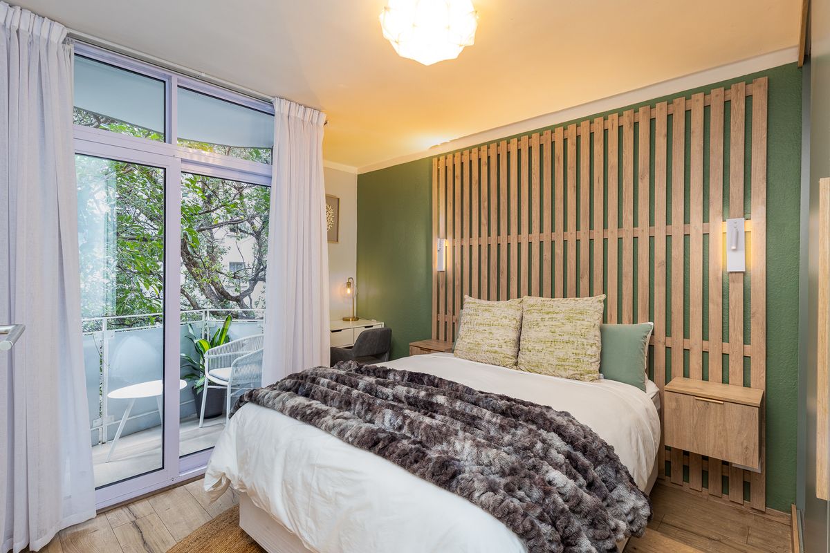A well-appointed bedroom featuring a decorative timber slat headboard, integrated bedside tables, and direct access to a private balcony through sliding glass doors.
