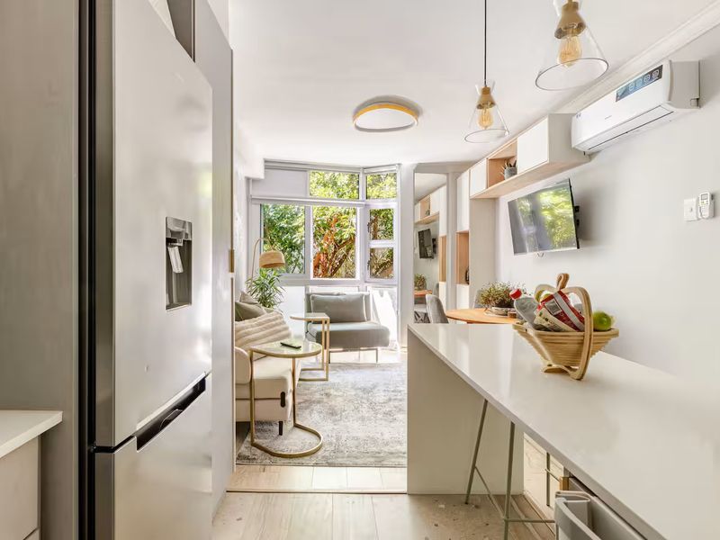 Modern open-plan living area featuring a sleek kitchen island, built-in cabinetry, split-system air conditioning, and large windows providing natural light and garden views.