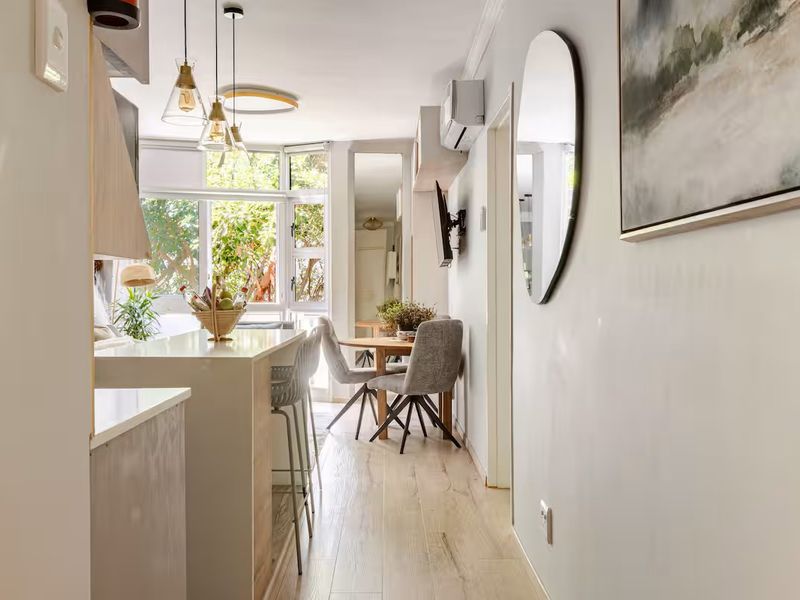 A bright open-plan living and kitchen area featuring modern laminate flooring, a central kitchen island, and large windows providing natural light.