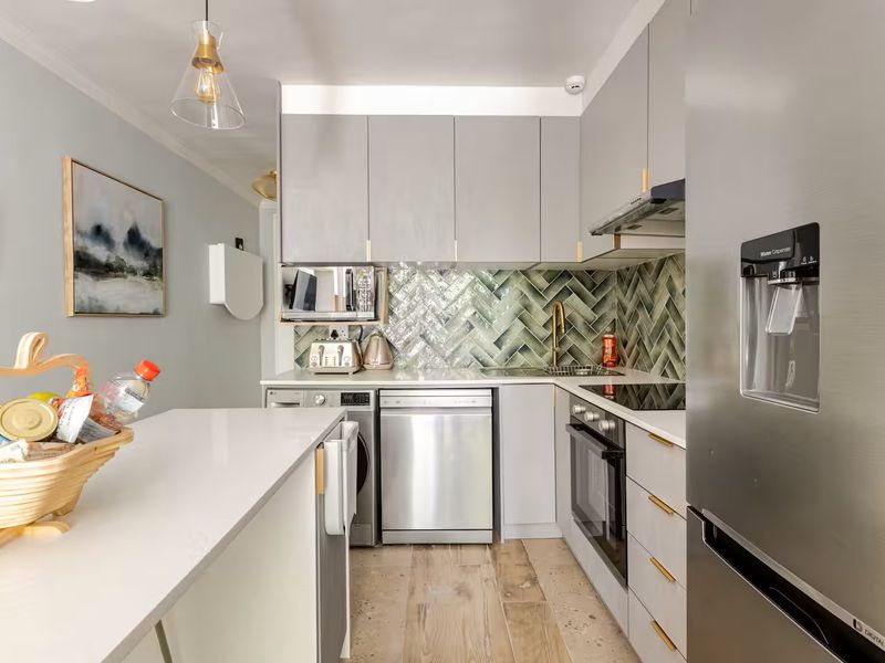 Modern kitchen featuring grey cabinetry, a stylish herringbone tile backsplash, stone countertops, and integrated appliances, offering a clean and contemporary aesthetic.