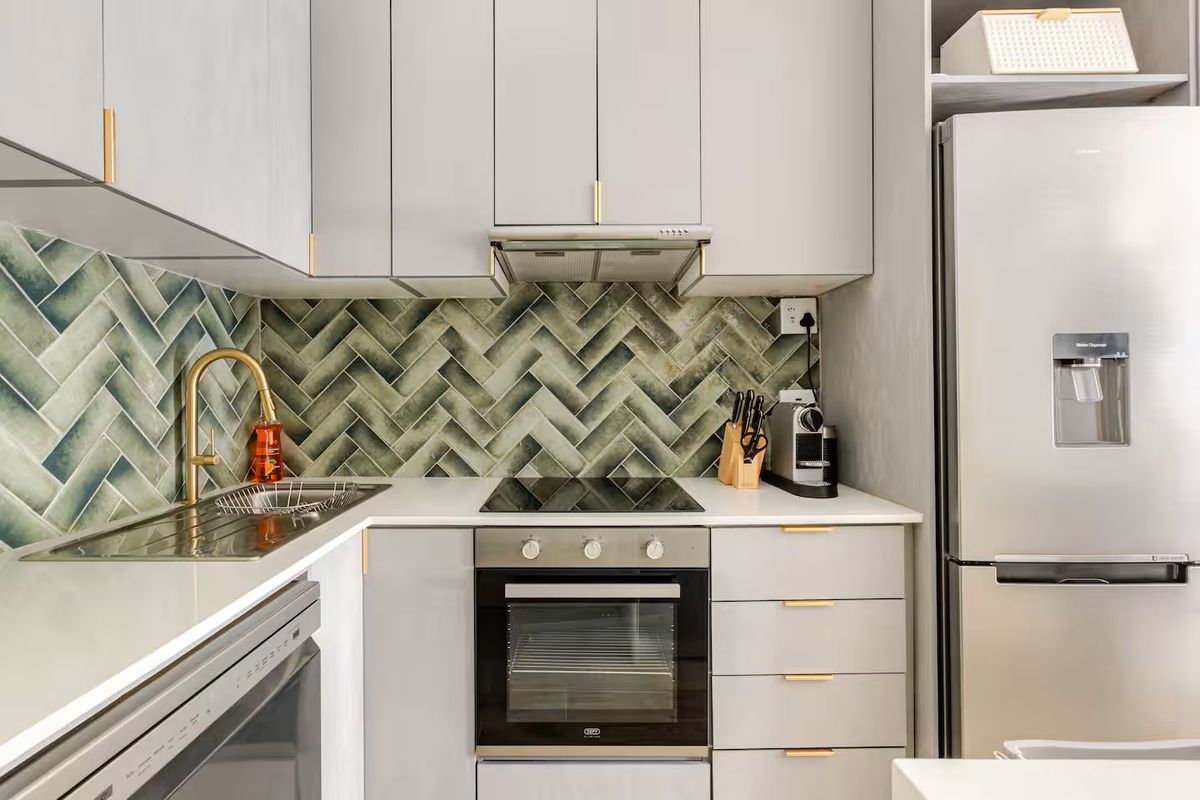 Modern kitchen featuring grey cabinetry, quartz countertops, a stylish green herringbone tile backsplash, and integrated stainless steel appliances.