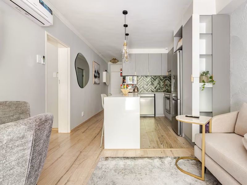 Modern open-plan living area featuring a sleek kitchen with herringbone backsplash, island bench, and light wood-look flooring throughout the combined space.