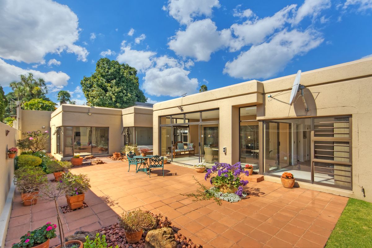 A spacious rear patio area featuring terracotta tiling, large sliding glass doors providing indoor-outdoor flow, and established garden beds.