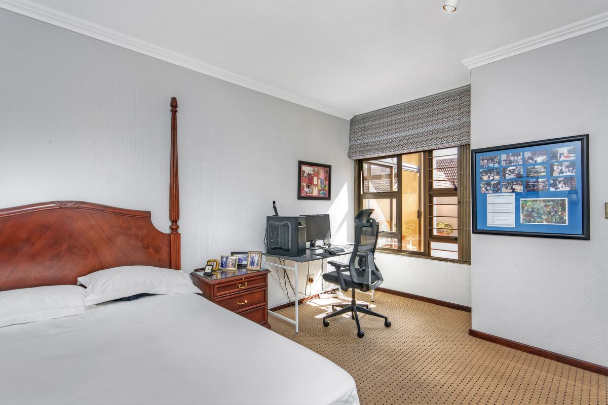 A functional bedroom featuring carpeted flooring, a window with security bars, and a fitted roman blind.