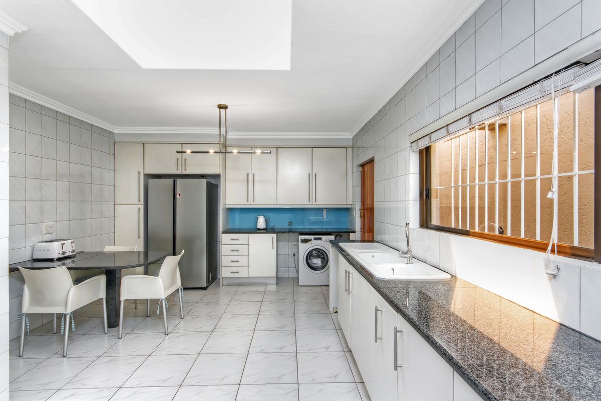 A functional kitchen featuring granite countertops, double basin sink, ample built-in cabinetry, tiled finishes, and a skylight for natural illumination.