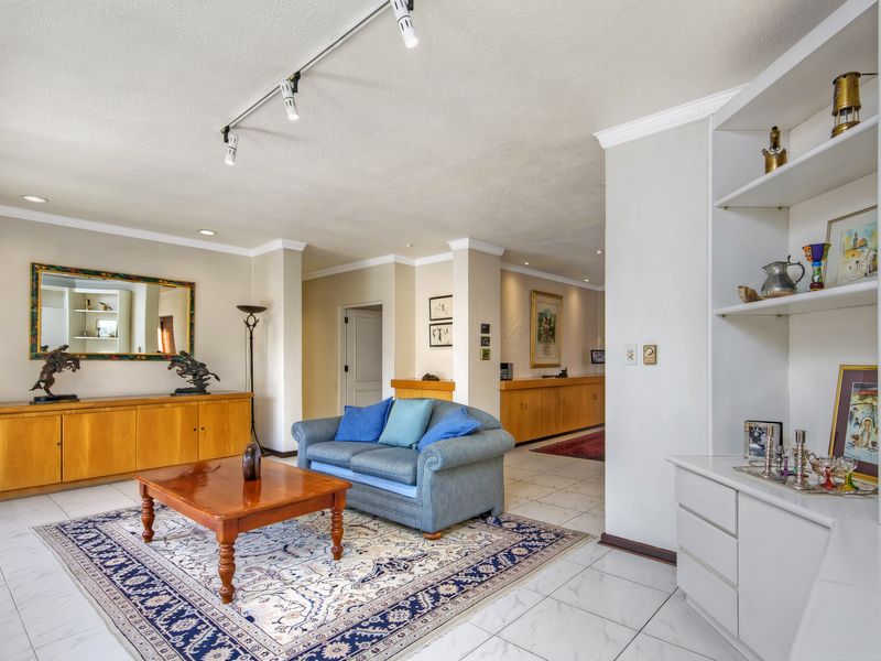 Spacious living area featuring tiled flooring, built-in cabinetry, and integrated shelving, illuminated by modern track lighting with a neutral color palette.