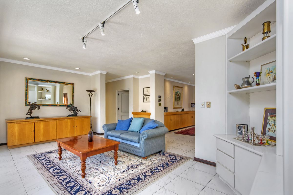 Spacious living area featuring tiled flooring, built-in cabinetry, and integrated shelving, illuminated by modern track lighting with a neutral color palette.