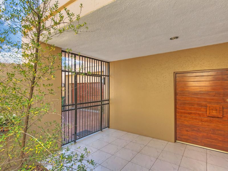 A covered entrance area featuring tiled flooring, a solid wood front door, and a secure metal gate.