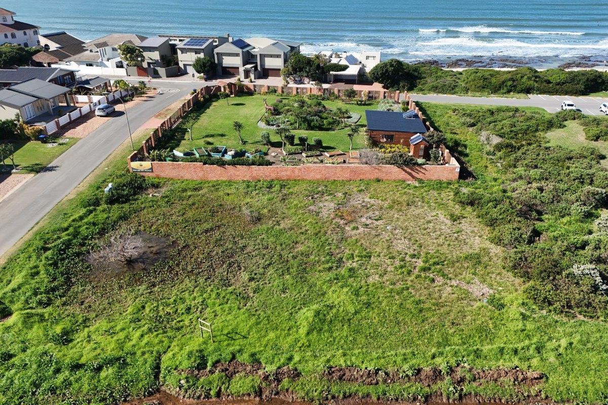 Aerial view of a vacant residential plot featuring a landscaped garden, perimeter brick walling, and a small outbuilding with solar panels near the coast.