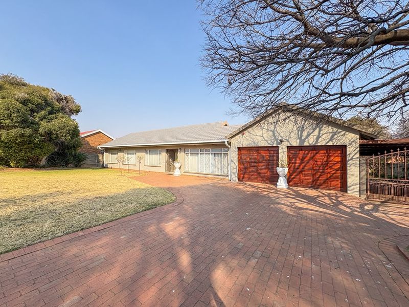 Front elevation of a single-story house featuring a brick-paved driveway, double wooden garage doors, and a well-maintained front lawn.