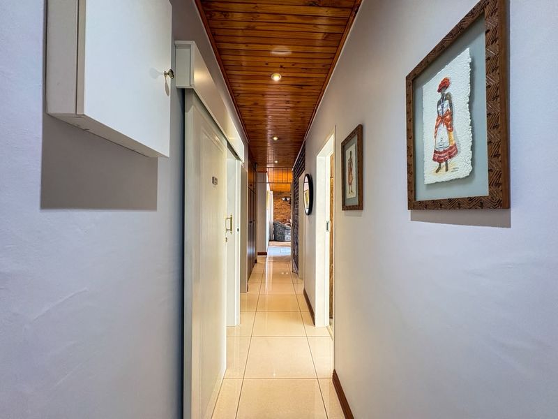 A well-lit hallway featuring tiled flooring and a warm timber tongue and groove ceiling, providing access to various rooms within the home.