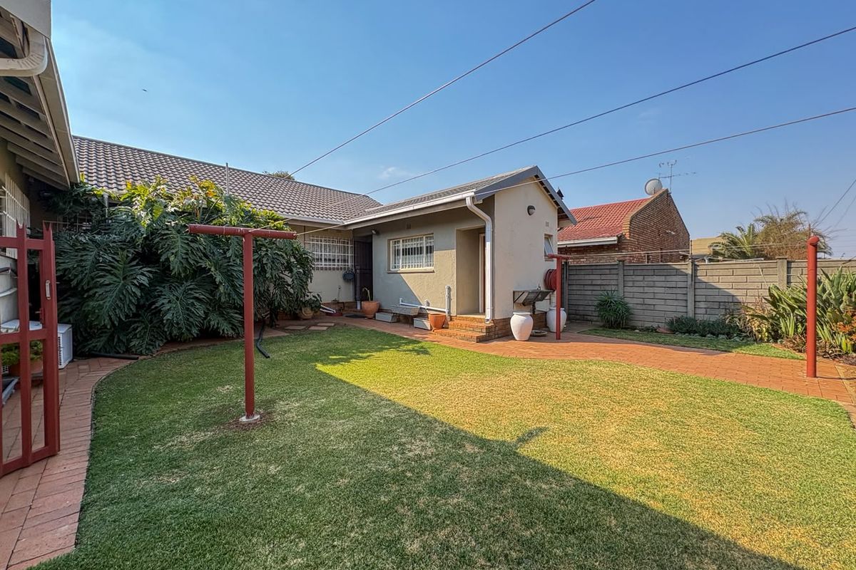 A well-maintained rear garden featuring a paved patio area, manicured lawn, and secure boundary walling.