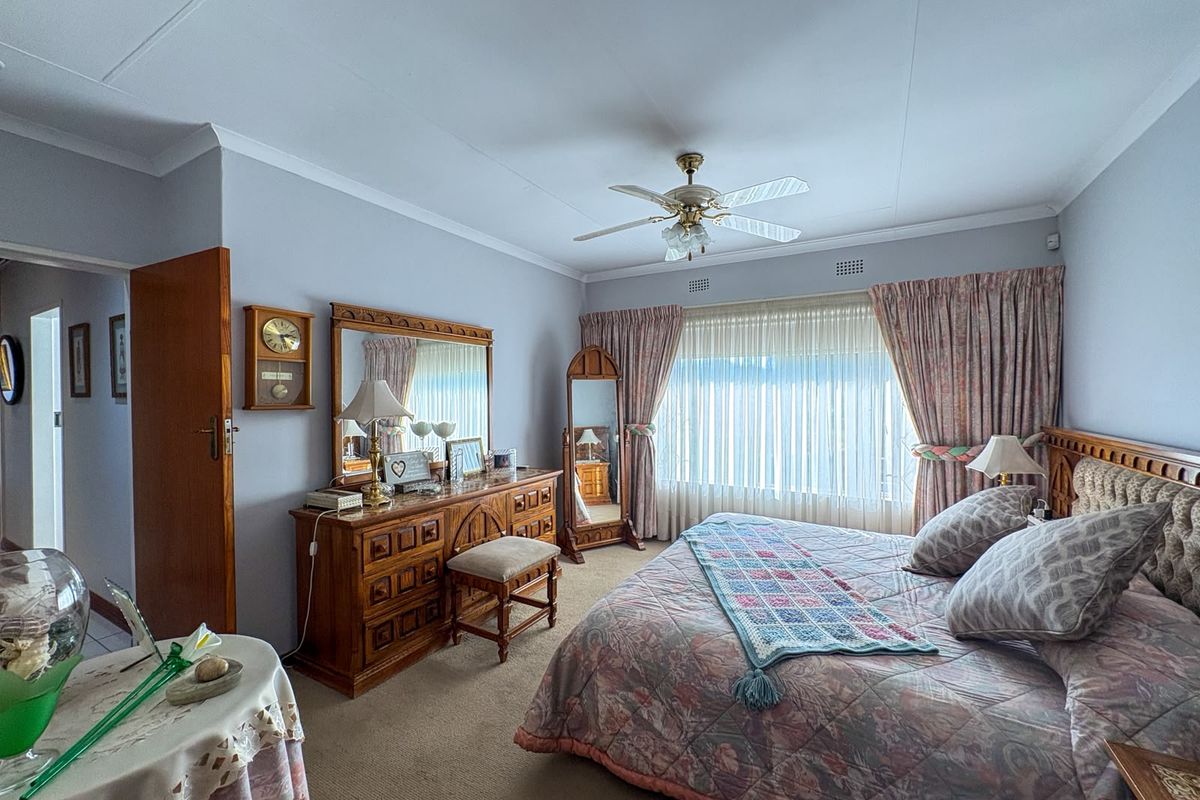 A spacious bedroom featuring carpeted flooring, a ceiling fan, and large windows with curtains.